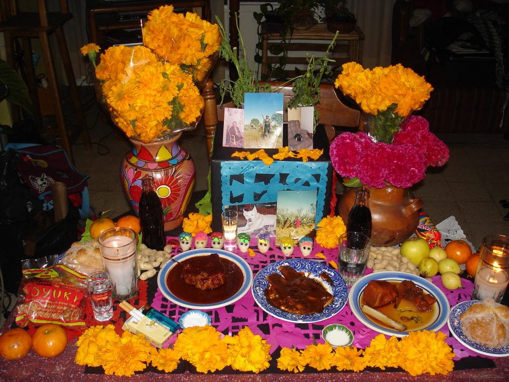 mexican day of the dead altar with offerings of food, sugar skulls, flowers and candles