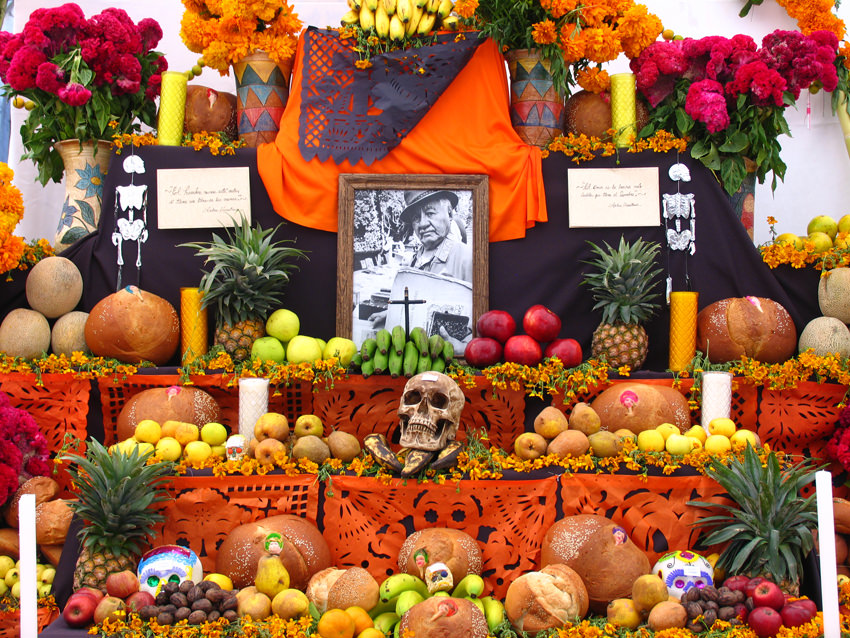 an altar for the day of the deqd with cut paper, candles, flowers, sugar skulls, skeletons, fruit, nuts, and bread.